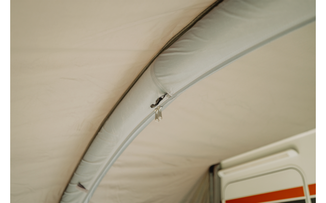 Binnenaanzicht van een stoffen dak met een gebogen, gestikte buis en een open rits met een klein metalen ritstrekker; rechts zichtbaar: een wit paneel met een oranje streep