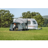 Witte caravan met aangebouwd voortent op een groen weiland, bomen op de achtergrond