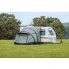 Witte caravan met grijs voortent op een groen veld, bomen op de achtergrond