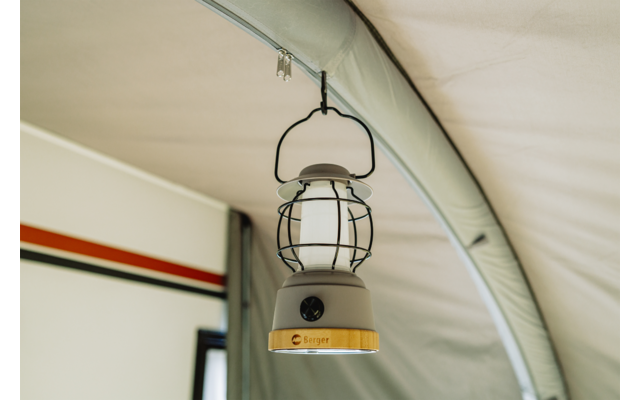 Een hangende lantaarn met metalen kooi aan een haak aan het tentdak; lichtgekleurde tentbinnenkant, zichtbare tentstok en een rechthoekig raam met een zwarte en rode streep