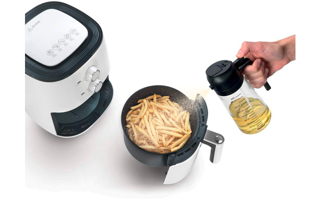 Weiße Heißluftfritteuse mit offenem Korb voller Pommes, Hand gießt Öl aus Glaskaraffe
