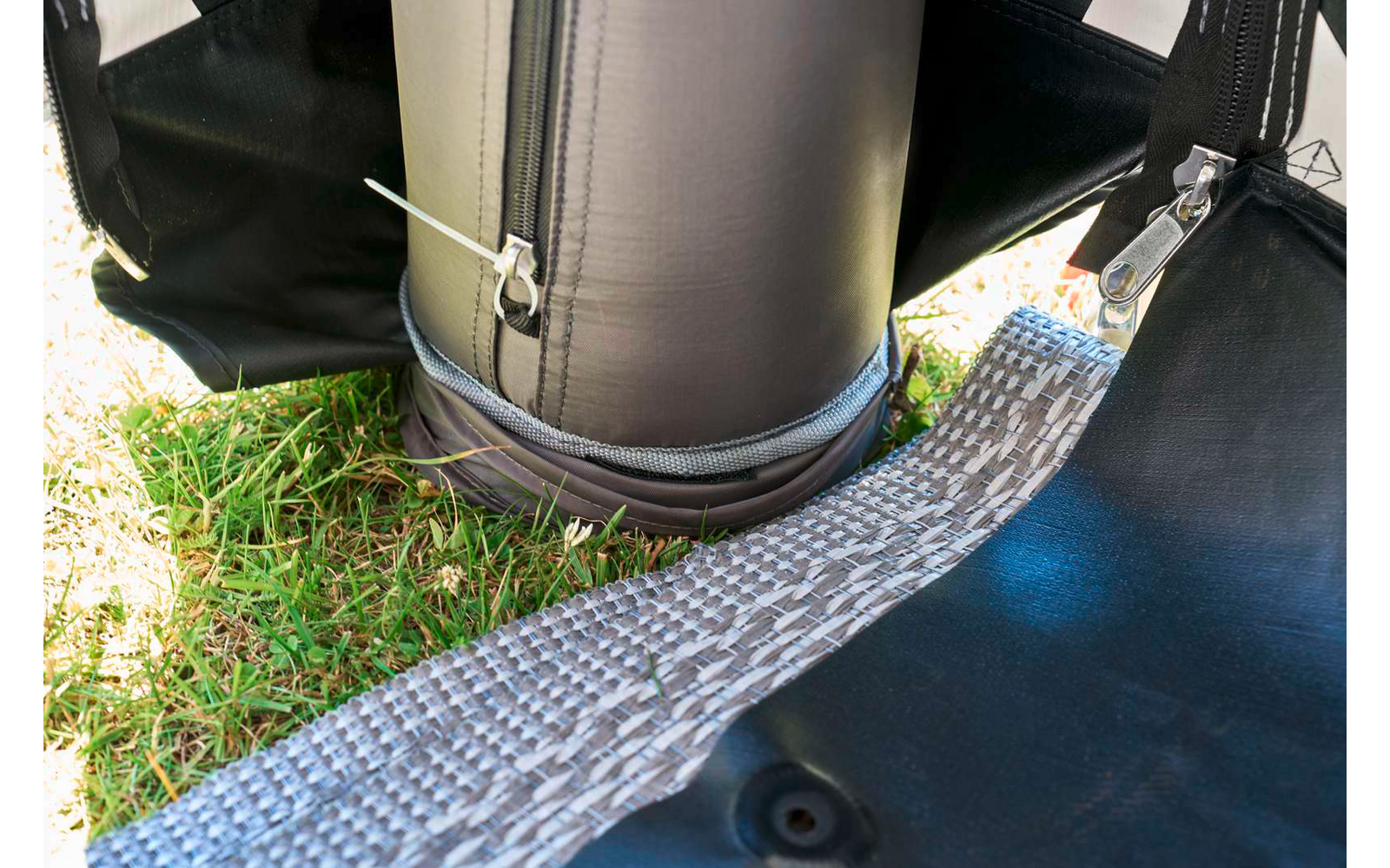 Unterer Bereich eines aufrechten schwarzen Zylinders mit Reißverschluss, befestigten Gurten und grauem, gewebtem Gurt auf Gras
