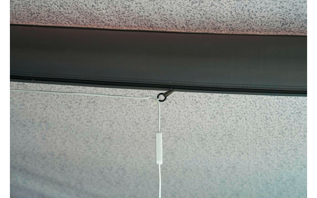 Weißes Zugband mit kleinem weißem Kunststoffzylinder hängt an einem schwarzen Haken an einem schwarzen Profil vor grauem, gesprenkeltem Stoff