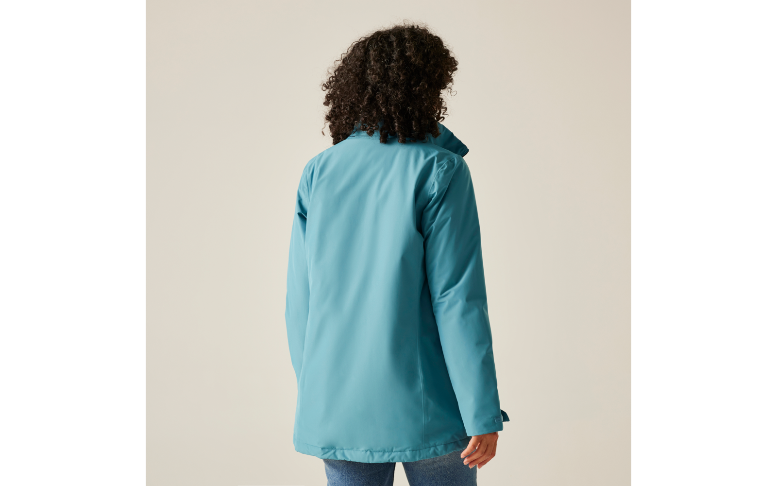Femme vue de dos portant une veste bleue sur un fond beige