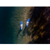 Luftaufnahme von zwei Personen auf blauen Stand-up-Paddleboards mit Paddeln über flachem Wasser, neben dunklen Algenflächen und sonnenbeleuchteten Wasserreflexen