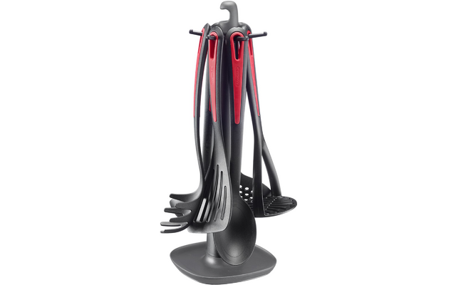 Soporte giratorio gris con seis utensilios de cocina de plástico gris oscuro con acentos rojos en los mangos, entre ellos un cucharón, una espumadera, un recogepastas, una espátula y una cuchara de cocina