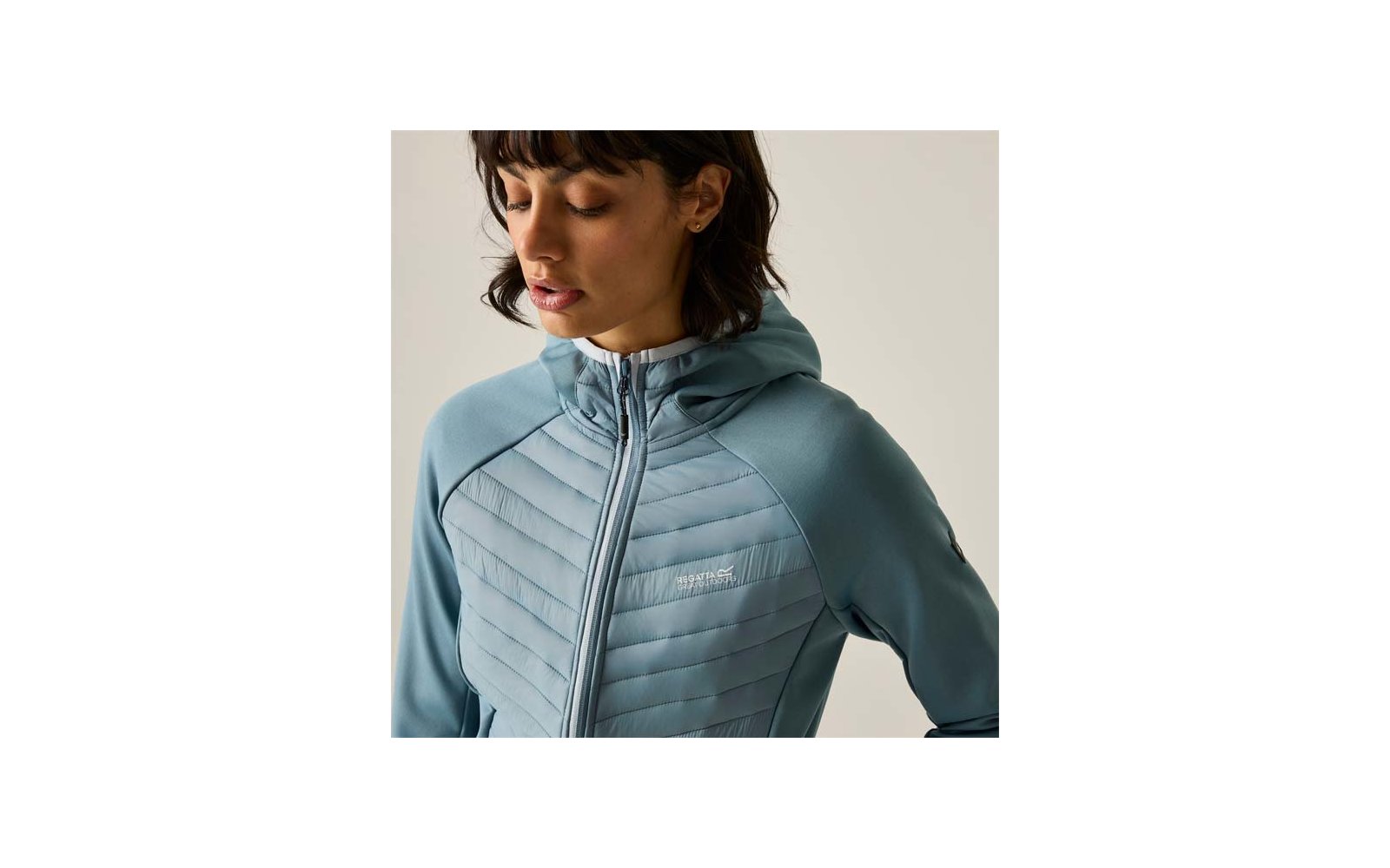 Person with short dark hair looking down, wearing light blue quilted jacket with hood, zipper and small chest logo