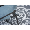 Close-up van een lichtblauwe meshzitting met grijs metalen frame en scharnier op een zwart-wit vloerkleed met bloemenpatroon