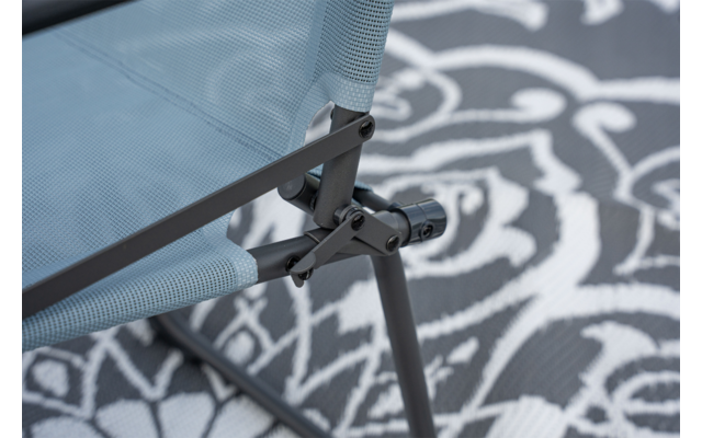 Close-up van een lichtblauwe meshzitting met grijs metalen frame en scharnier op een zwart-wit vloerkleed met bloemenpatroon