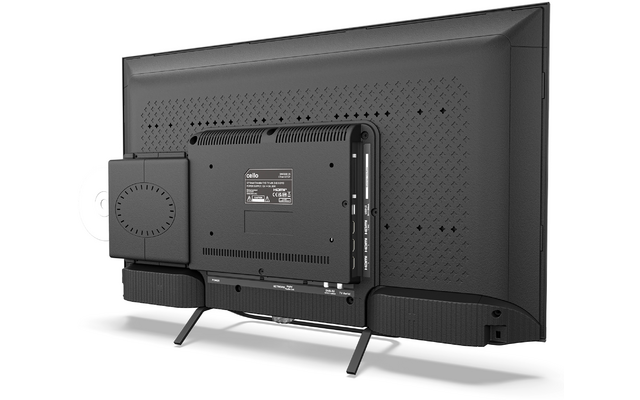 Achteraanzicht van een zwarte flatscreen op twee pootjes, met links een klein rechthoekig apparaat bevestigd, geperforeerde ventilatie op de achterzijde, twee langgerekte modules onderaan en zichtbare aansluitingen rechts