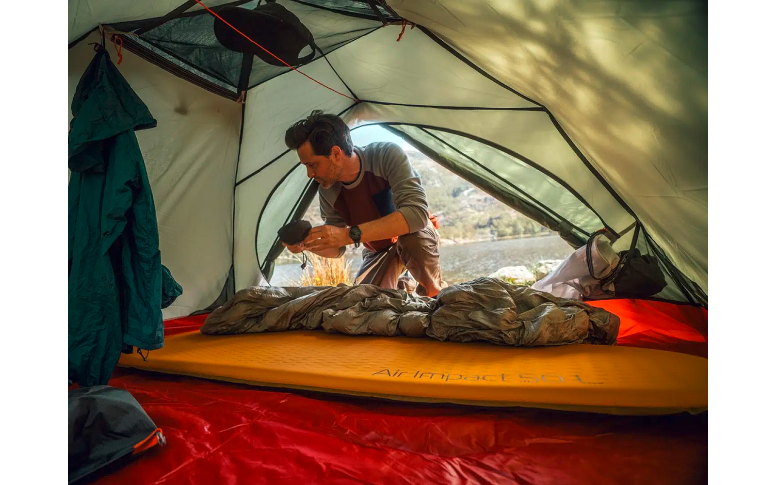 Person kniet in einem Zelt und organisiert Gegenstände auf einer Isomatte