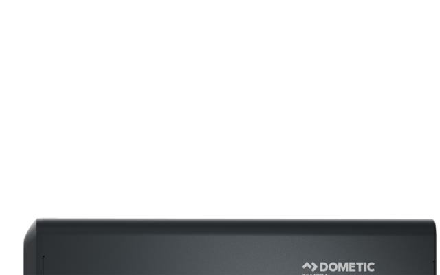 Dunkelgraues rechteckiges Gehäuse mit Dometic-Logo oben, zwei Anschlussklemmen links (rot und schwarz) und zwei Klappen an der unteren Vorderseite
