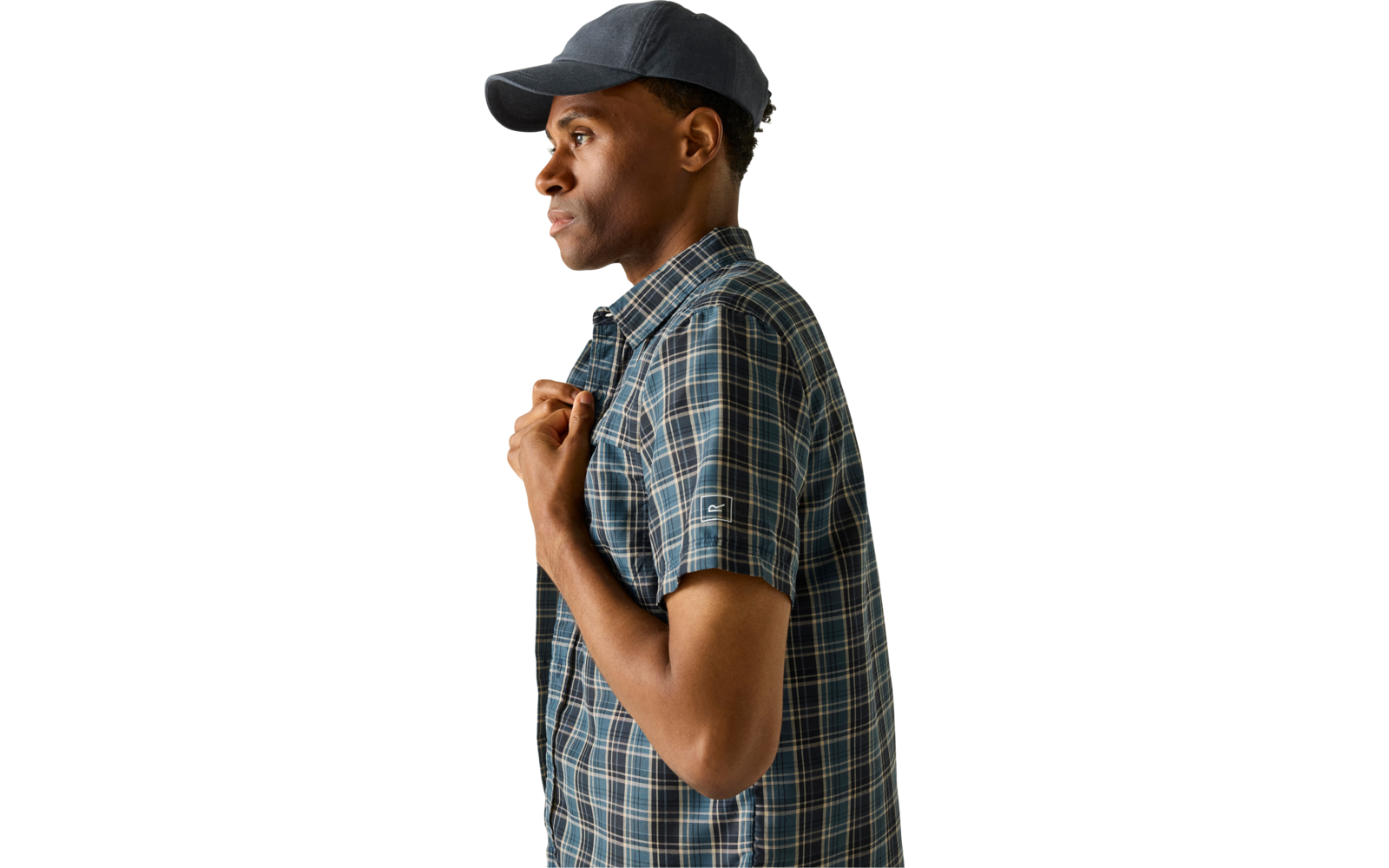 Person im Profil mit dunkelblauer Kappe und kurzärmligem blau kariertem Hemd, hält das Hemd am Kragen vor einfarbigem beigem Hintergrund