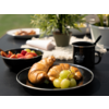Assiette avec croissants et raisins, tasse noire et bol de confiture en arrière-plan sur une table noire