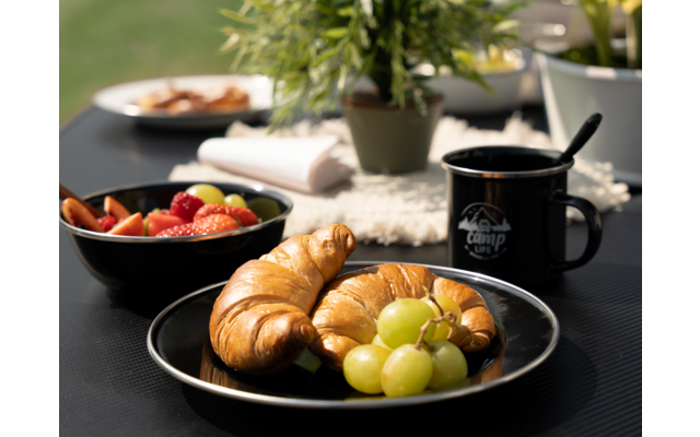 Assiette avec croissants et raisins, tasse noire et bol de confiture en arrière-plan sur une table noire