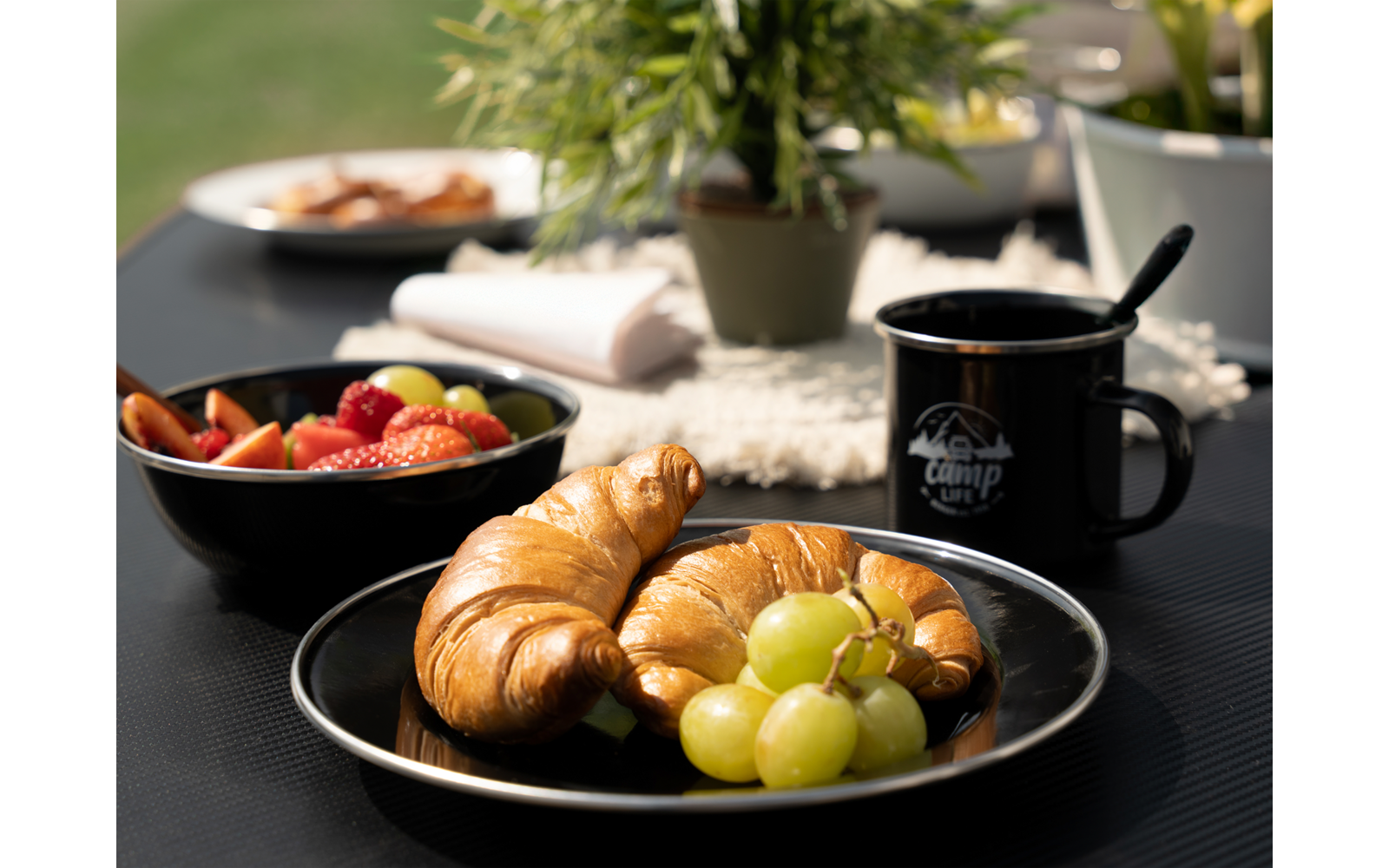 Assiette avec croissants et raisins, tasse noire et bol de confiture en arrière-plan sur une table noire