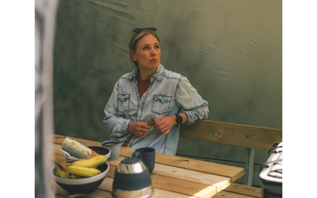 Frau sitzt an einem Holztisch mit Obst und Tassen und schaut nach rechts