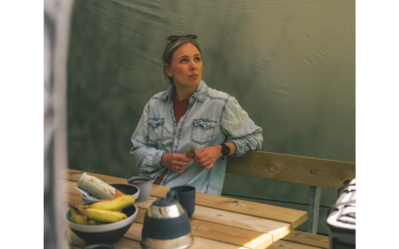 Frau sitzt an einem Holztisch mit Obst und Tassen und schaut nach rechts