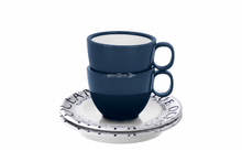 Deux tasses en céramique bleu foncé empilées avec anses à droite sur une soucoupe blanche avec texte bleu, petite cuillère métallique, fond blanc