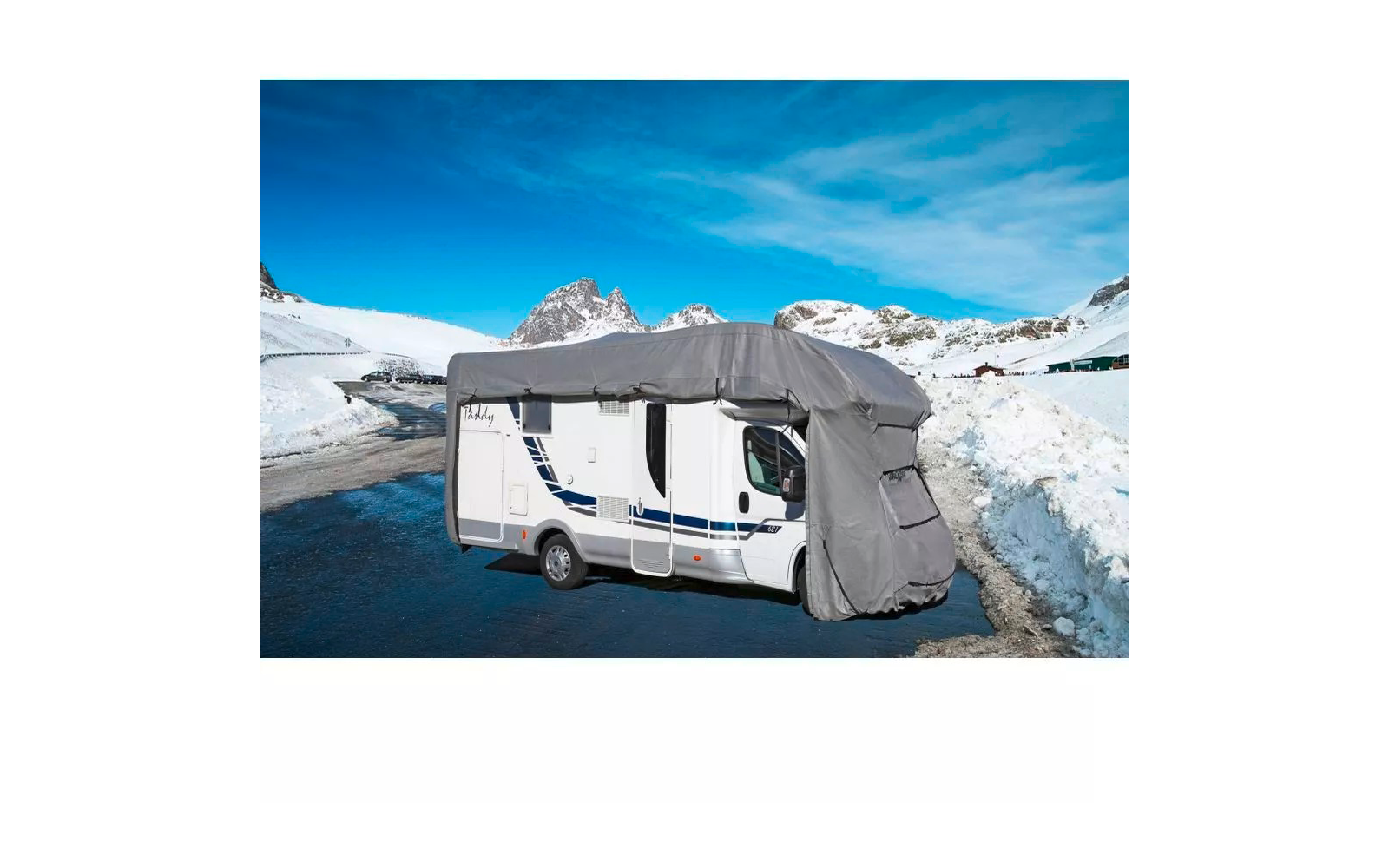 Weißes Wohnmobil mit grauer Abdeckung an der Front, auf einer schneebedeckten Bergstraße mit Schneehaufen und blauem Himmel