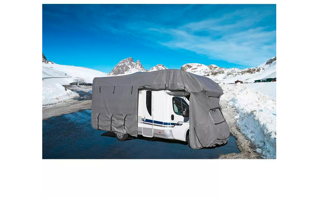 Wohnmobil mit grauer Abdeckung auf verschneiter Bergstraße, schneebedeckte Berge und blauer Himmel im Hintergrund