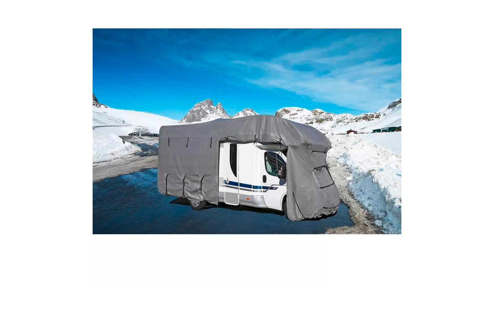 Wohnmobil mit grauer Abdeckung auf verschneiter Bergstraße, schneebedeckte Berge und blauer Himmel im Hintergrund