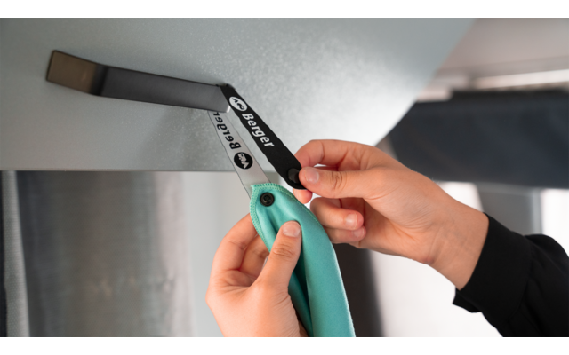 Zwei Hände halten den Griff eines türkisfarbenen Rasiermessers und eine schwarze Metallklinge mit weißer Beschriftung vor einer hellgrauen Oberfläche