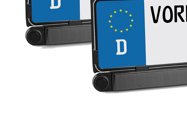 Gros plan de deux plaques d'immatriculation, bande bleue avec étoiles jaunes et lettre blanche 'D', lettres noires partiellement visibles 'VOR' sur fond blanc, support en plastique noir en bas