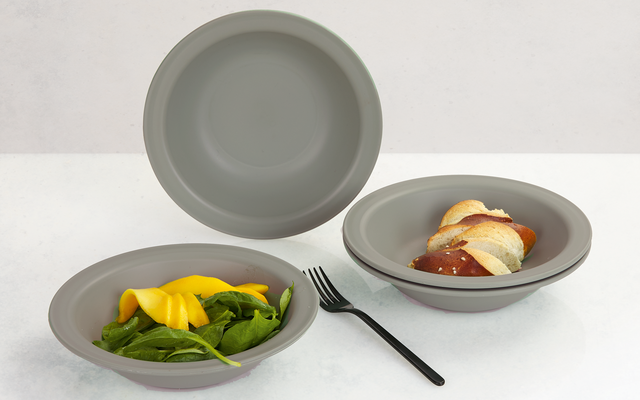 Two gray bowls with dessert, one containing mango and spinach leaves, the other with apple slices, a black spoon beside them