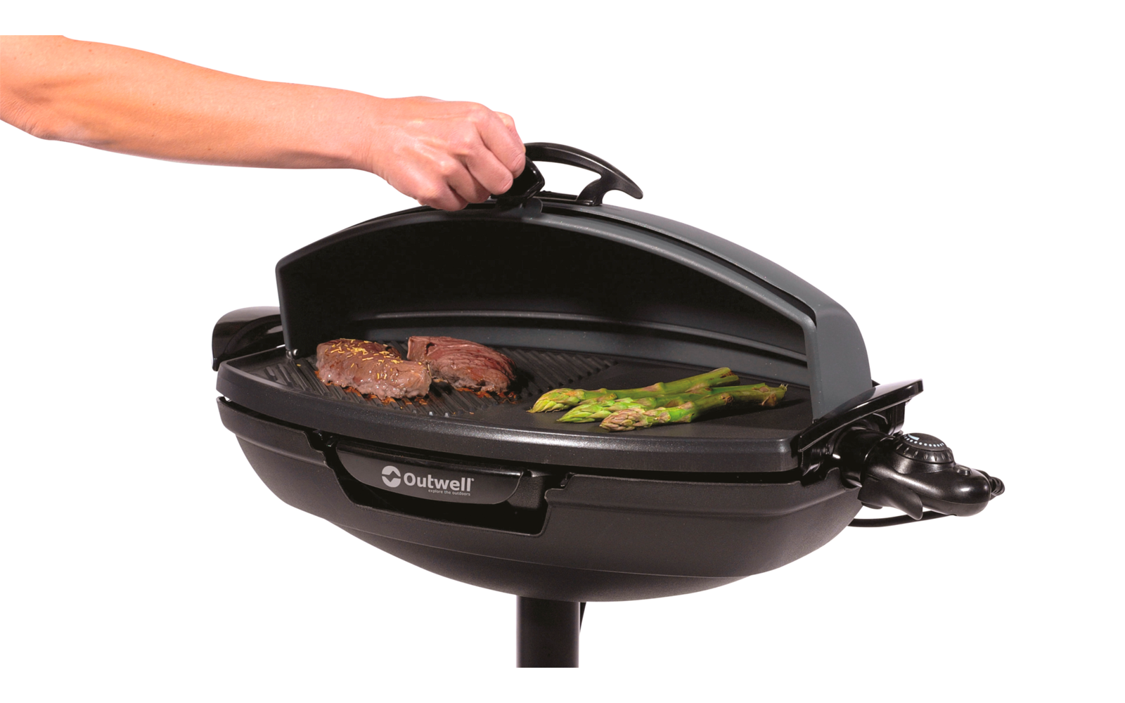 Hand hebt den Deckel eines schwarzen Grills, auf dem Fleisch und grünes Gemüse liegen