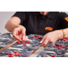 Hände über grauen Kunststoffplatten mit roten Verbindungsteilen auf einem Tisch; schwarzes Poloshirt mit orangefarbenem Logo sichtbar