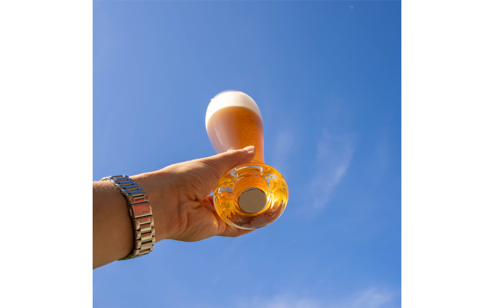 Hand hält ein Glas Bier vor blauem Himmel