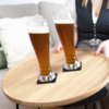 Zwei gefüllte Biergläser auf einem runden Holztablett, weibliche Person im Dirndl im Hintergrund