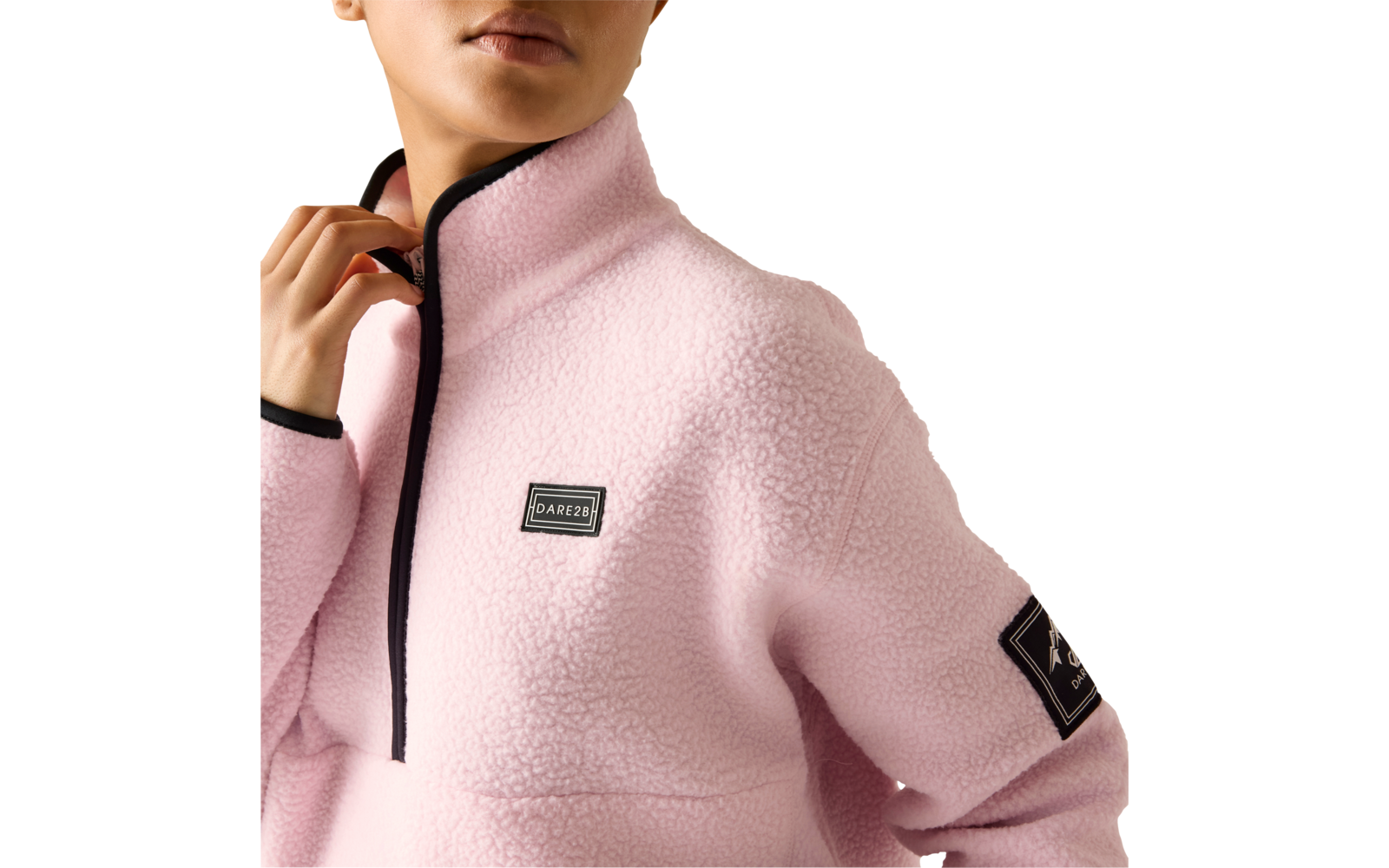 Oberkörper einer Person mit hellrosa Fleecejacke, schwarzem Reißverschluss und Kanten, rechteckiges Label auf der Brust und Patch am Ärmel; Hand hält den Kragen, Gesicht teilweise abgeschnitten