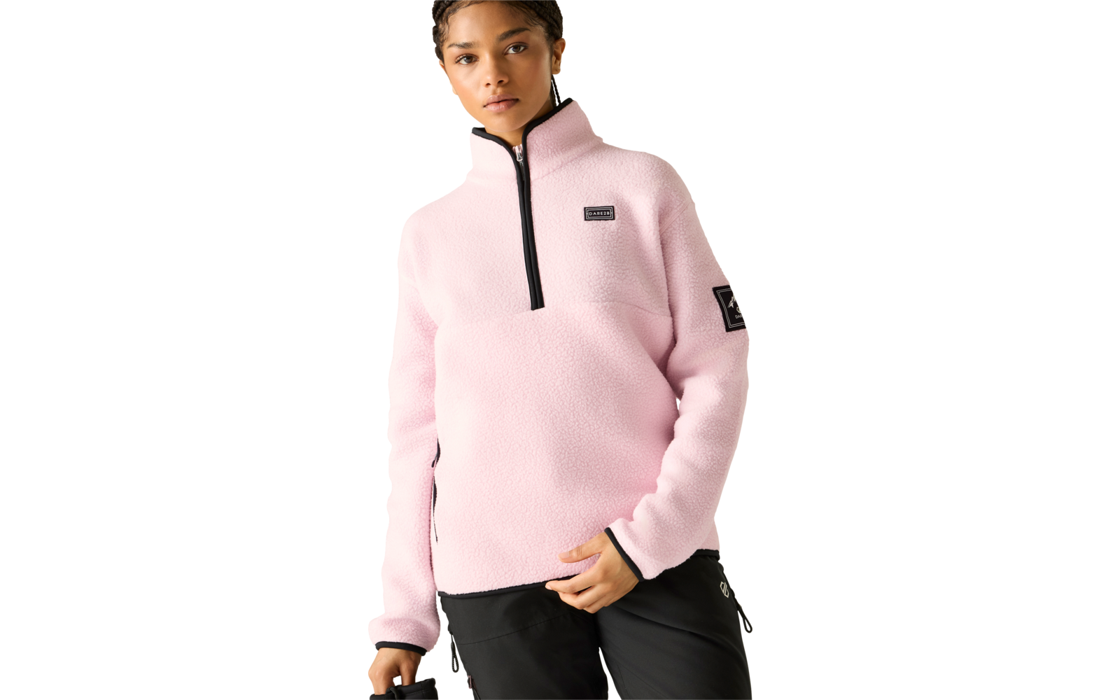 Person trägt hellrosa Fleece-Pullover mit kurzem schwarzem Reißverschluss, rechteckigem Patch auf der Brust, quadratischem Patch am linken Oberarm und schwarze Hose