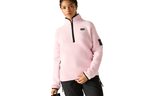 Person trägt hellrosa Fleece-Pullover mit kurzem schwarzem Reißverschluss, rechteckigem Patch auf der Brust, quadratischem Patch am linken Oberarm und schwarze Hose