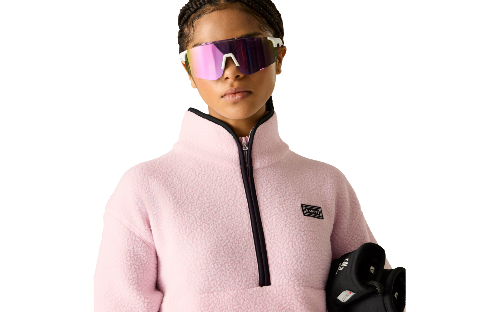 Person mit geflochtenem Haar, rosa Fleecejacke mit halbem Reißverschluss, verspiegelte violette Sonnenbrille, hält ein schwarzes Objekt mit sichtbarem weißem Etikett