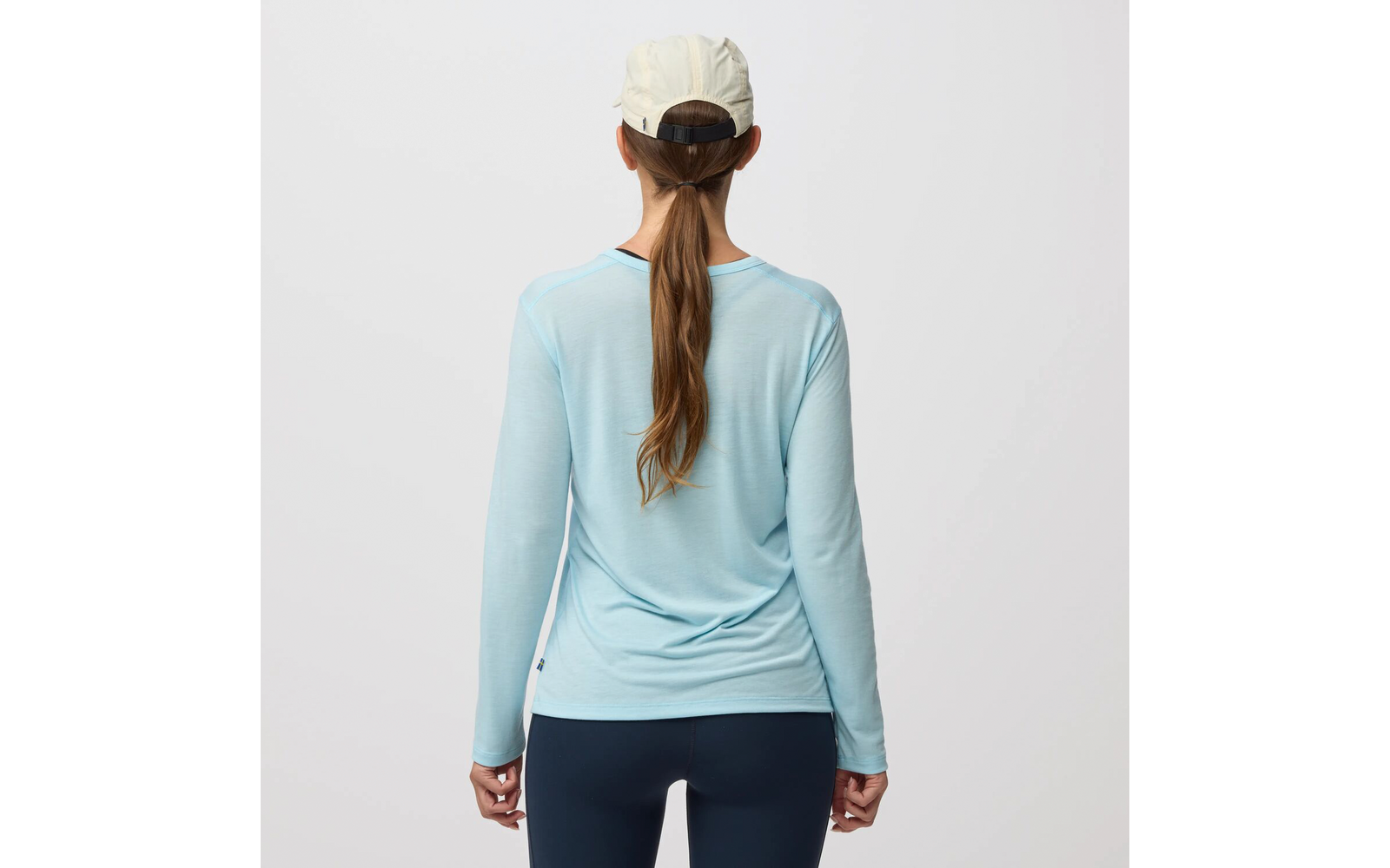 Persona de espaldas con camiseta de manga larga azul claro, mallas azul oscuro, gorra clara y una larga cola de caballo