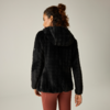 Persona vista de espaldas, lleva una chaqueta con capucha negra de textura aterciopelada y leggings marrón rojizo, pelo recogido en un moño suelto, fondo liso y claro