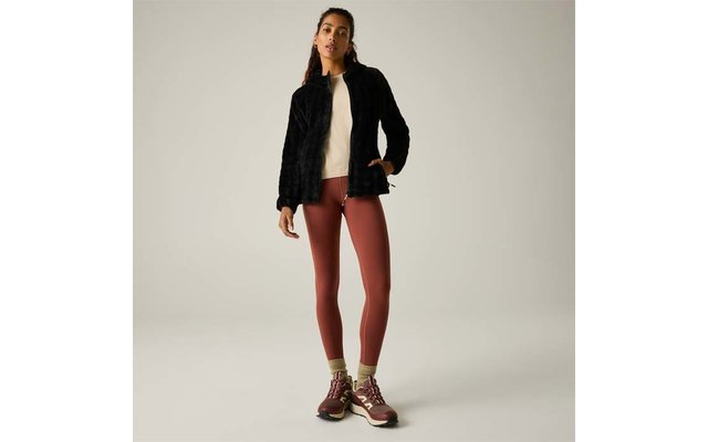 Mujer, cuerpo entero visible, lleva chaqueta negra de pelo sintético, suéter claro, mallas color óxido, zapatillas de senderismo burdeos y calcetines amarillos sobre fondo liso