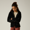 Persona con el pelo recogido lleva una chaqueta polar negra, brazos cruzados, mira hacia abajo, camiseta clara y leggings color óxido sobre fondo gris claro