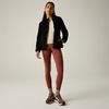 Mujer, cuerpo entero visible, lleva chaqueta negra de pelo sintético, suéter claro, mallas color óxido, zapatillas de senderismo burdeos y calcetines amarillos sobre fondo liso