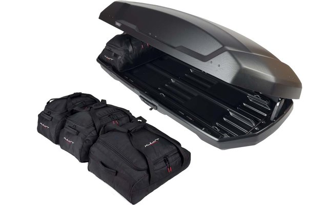 Offene schwarze Dachbox mit sichtbarem Innenraum, daneben drei schwarze Reisetaschen