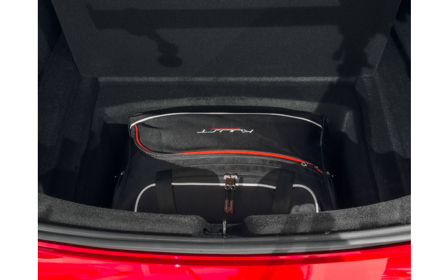 Compartiment noir rembourré avec insertions en mousse, bord rouge du véhicule en bas, sac de voyage noir avec liseré rouge et logo blanc, sangle visible avec boucle métallique