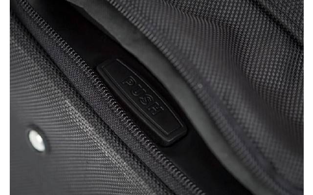 Gros plan d'une fermeture éclair noire sur un sac, partiellement ouverte, avec une tirette en plastique noir portant l'inscription 'PUSH' et tissu texturé