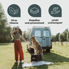 Frau mit Hut und roten Hosen steht neben Hund, der auf einer schwarzen Box vor einem hellblauen Campingbus sitzt; darüber drei runde Icons mit Blattsymbolen und den Texten "Ohne Chemie", "Stapelbar und systematisch", "Leicht und kompakt"; Picknickdec