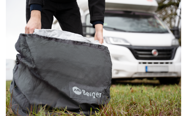 Hands of a person holding a gray packing bag with the 'Berger' logo; a white motorhome in the background; grass in the foreground