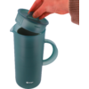 Main avec manche en maille marron soulève le couvercle d'une carafe verte avec poignée; logo Berger en bas à l'avant