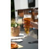 Hand houdt een glas bier buitenshuis vast, vervaagde stoelen en tafels op de achtergrond