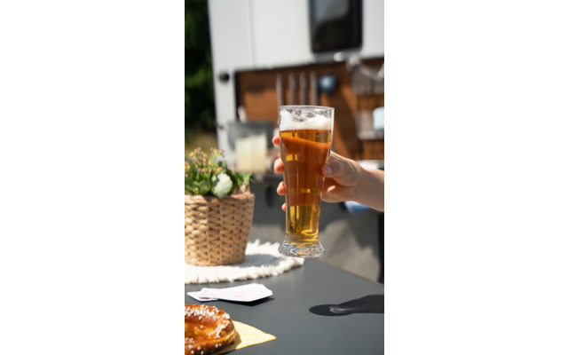 Hand houdt een glas bier buitenshuis vast, vervaagde stoelen en tafels op de achtergrond